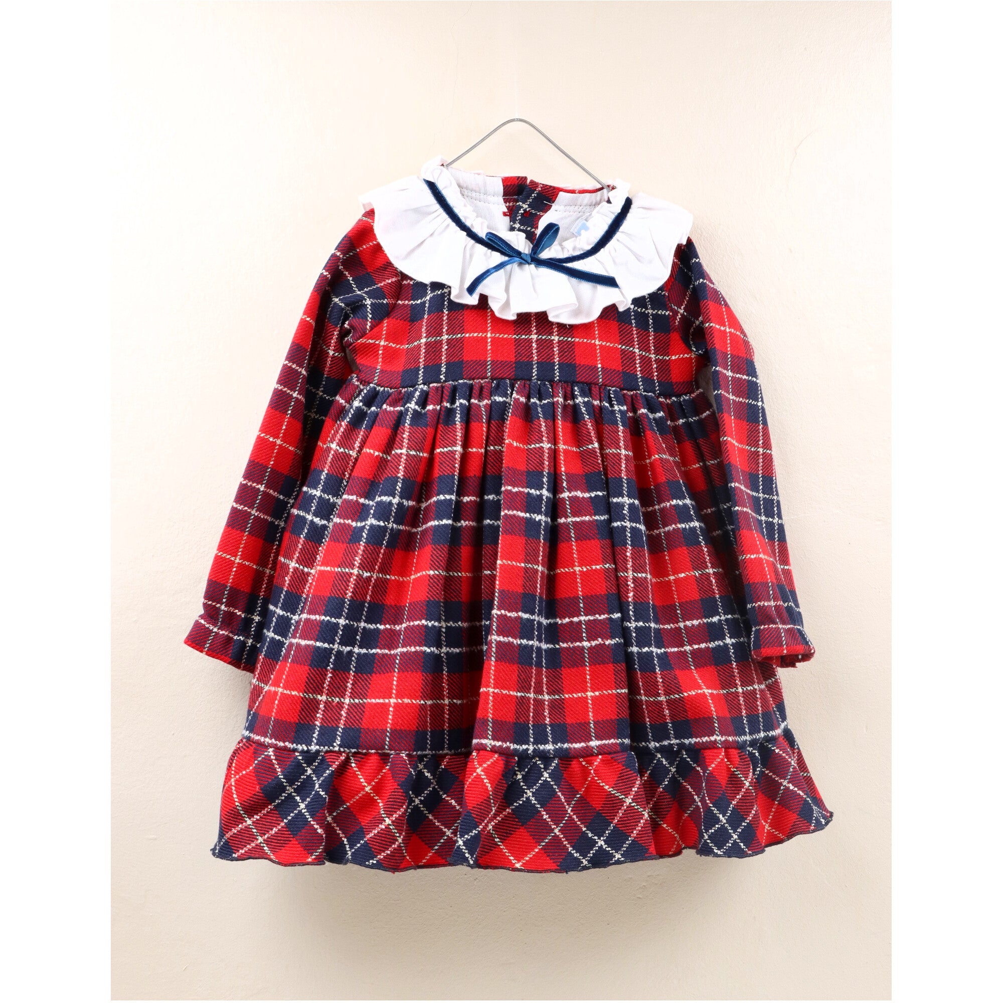 Abitino invernale per bambina in tessuto scozzese rosso con colletto bianco a volant e fiocchetto blu. Manica lunga, chiusura con bottoni sul retro e balza sul fondo per un look elegante e festivo. Perfetto per Natale ed eventi speciali